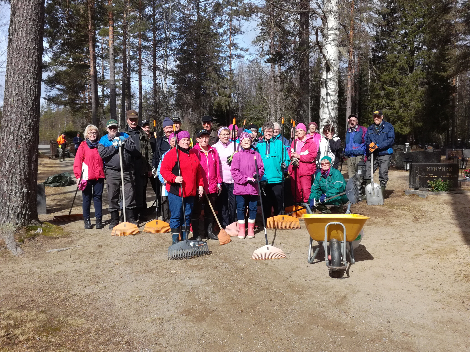 Sukevan hautasumaatalkoolaisia auringonpaisteessa hautausmaalla haravoineen ryhmäkuvassa.