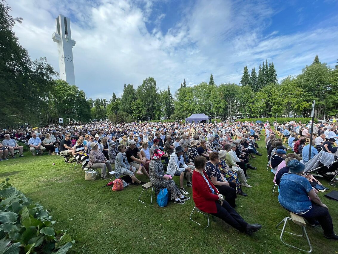 Herättäjäjuhlakansaa istumassa nurmikentällä pitkillä penkeillä.