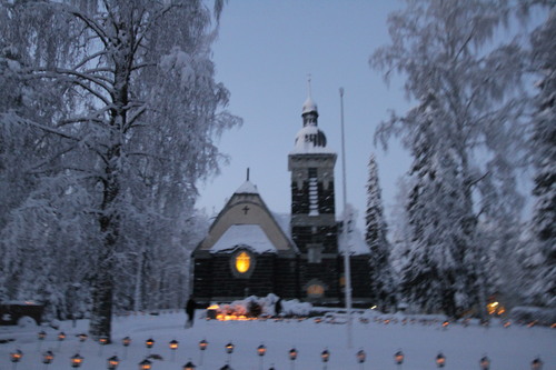 Sonkajärven kirkko ulkoapäin talvella. Hautausmaalla palaa kynttilöitä.