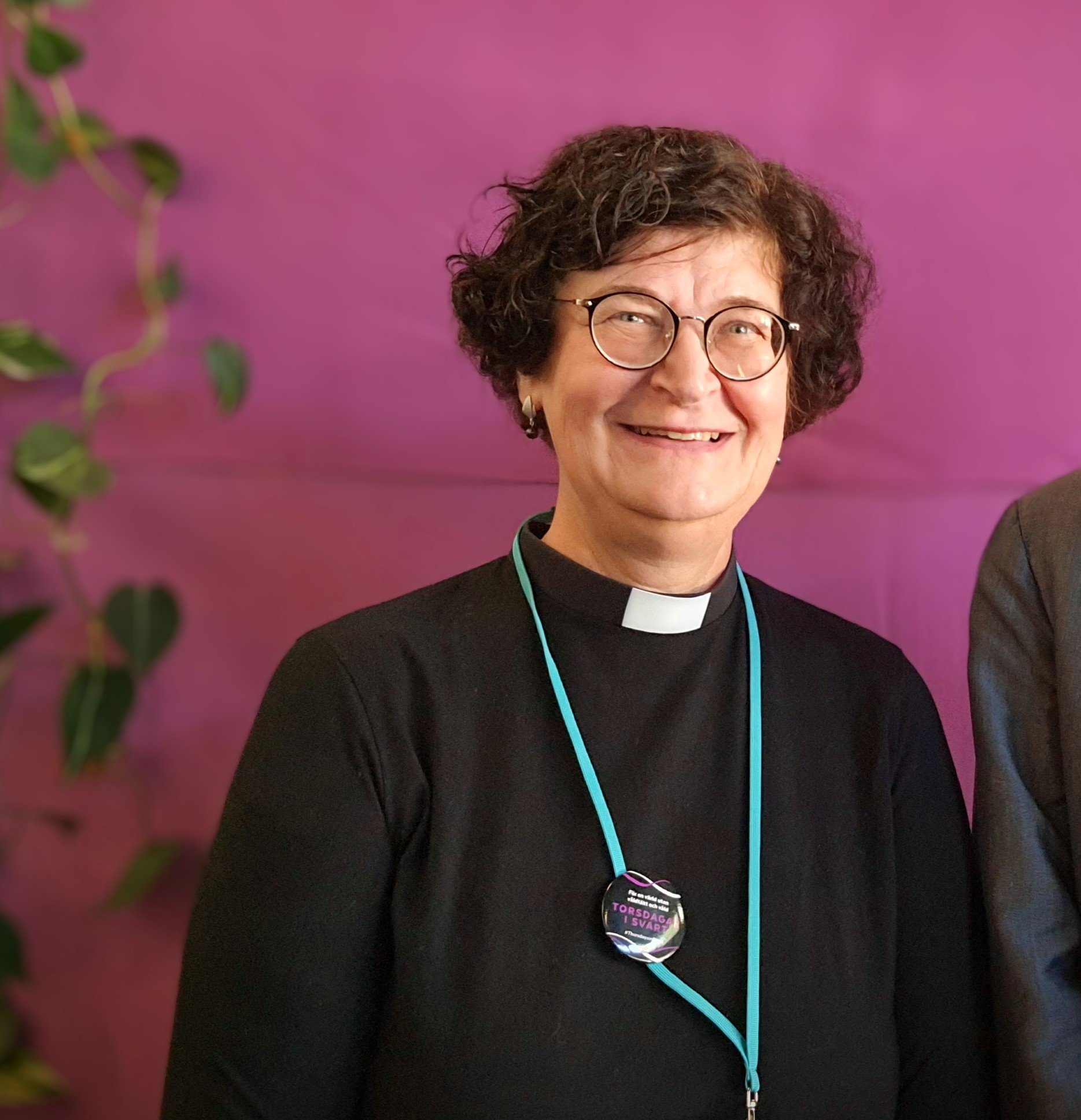 Tummassa papinpuvussaan oleva henkilö purppuran väristä taustaa vasten.
